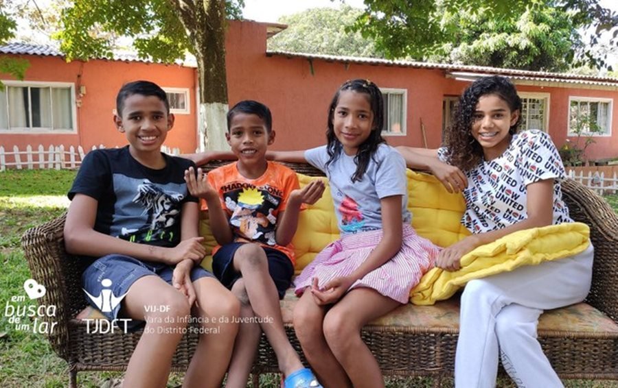 Dois meninos e duas meninas sentados em sofá em frente de casa laranja