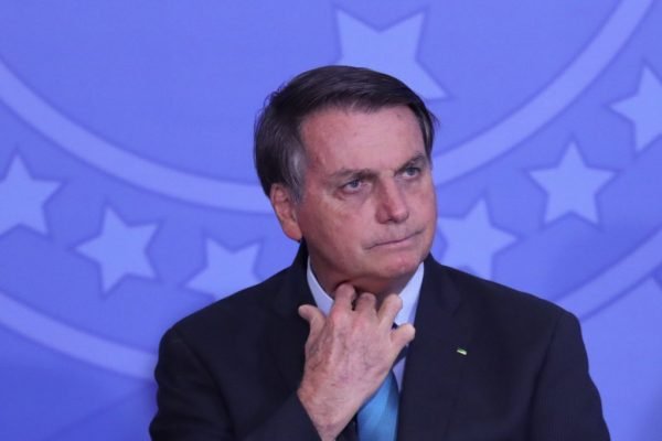 O presidente Jair Bolsonaro ajusta a gravata em cerimônia no Palácio do Planalto, com semblante sério e olhando para o lado - Metrópoles