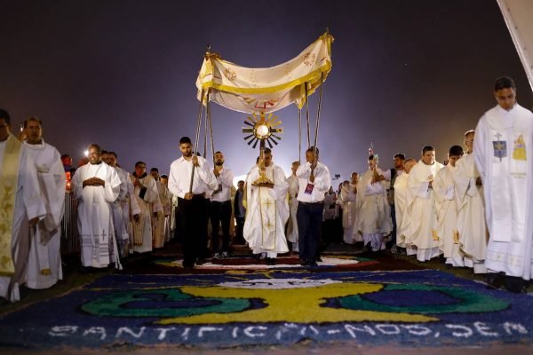 Peregrinação na Esplanada em comemoração ao Corpus Christi. Sob um tapete estampado, religiosos de batina passam segurando símbolos religiosos - Metrópoles