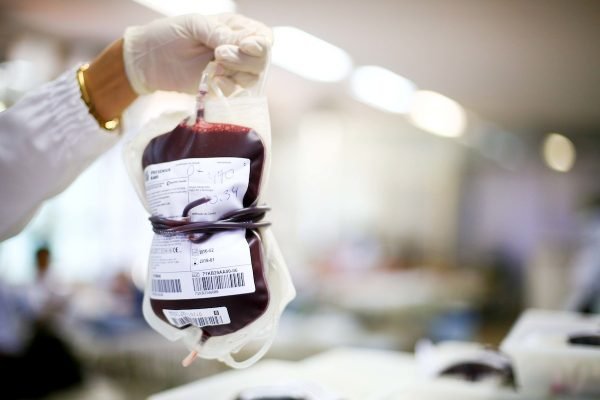Foto colorida de enfermeiro(a) usando luvas para segura bolsa de sangue