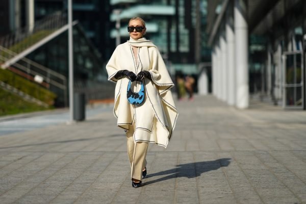Mulher usa look de tons claros, com cachecol. luvas pretas, bolsa pequena e óculos escuros, no street style