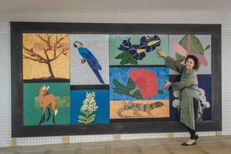 foto colorida de um painel com desenhos em mosaico, e a frente uma mulher apontando para o painel