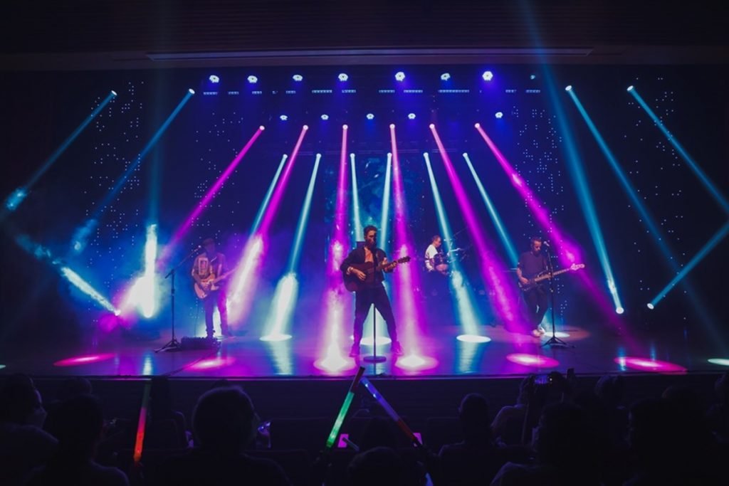 banda em palco iluminado com luzes roxas e azuis