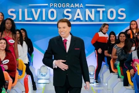O apresentador Sílvio Santos caminha entre plateia de seu programa, sorrindo e usando terno - Metrópoles