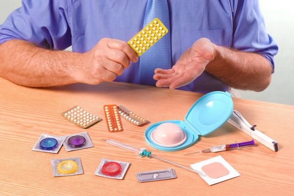 Foto de um homem em frente a uma mesa com vários métodos contraceptivos