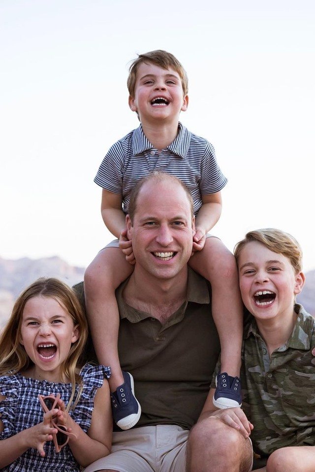 Foto colorida. Homem branco com duas crianças ao lado e um menino sentados em seus ombros