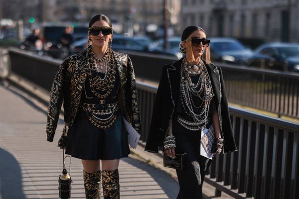 No street style, duas mulheres usam looks pretos com vários colares de pérolas, além de óculos escuros e cabelos presos com coque