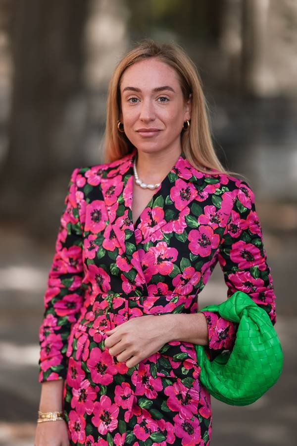 No street style, mulher loira usa roupa com estampa floral, bolsa verde e colar de pérolas