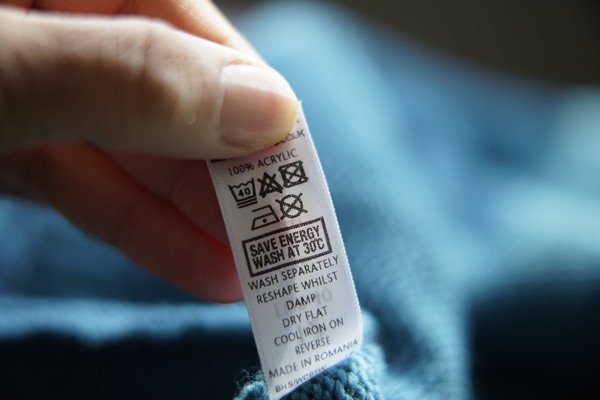 Etiqueta com instruções sobre lavagens e descritivo do material. A etiqueta está costurada em uma peça de roupa na cor azul