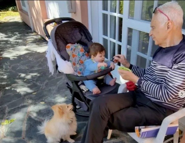 Homem idoso, de cabelo branco, brincando com bebê enquanto ele está em seu carrinho