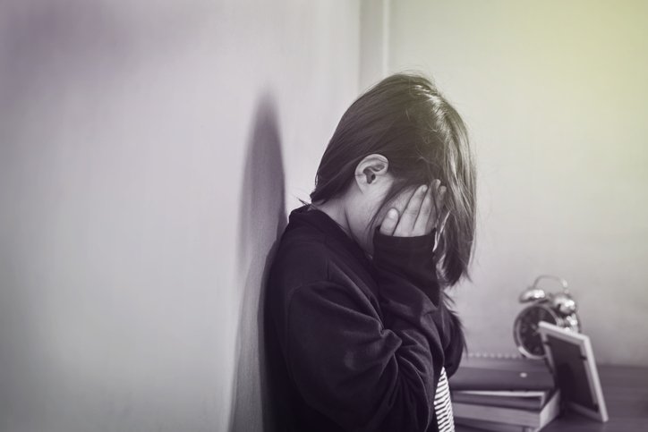 Criança encostada na parede com as mãos no rosto - Metrópoles