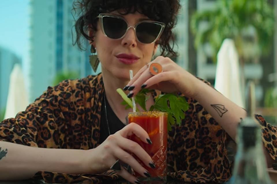 foto colorida de mulher usando óculos de sol, tomando um drink