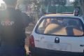 policial militar de costas e diante de um Corsa branco com a placa borrada
