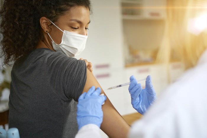 Woman with tied hair and gray blouse getting vaccinated - Metropolis