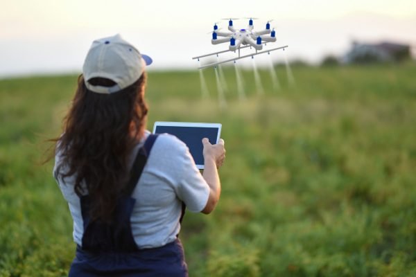 Imagem colorida de mulher pilotando drone em lavoura- Metrópoles