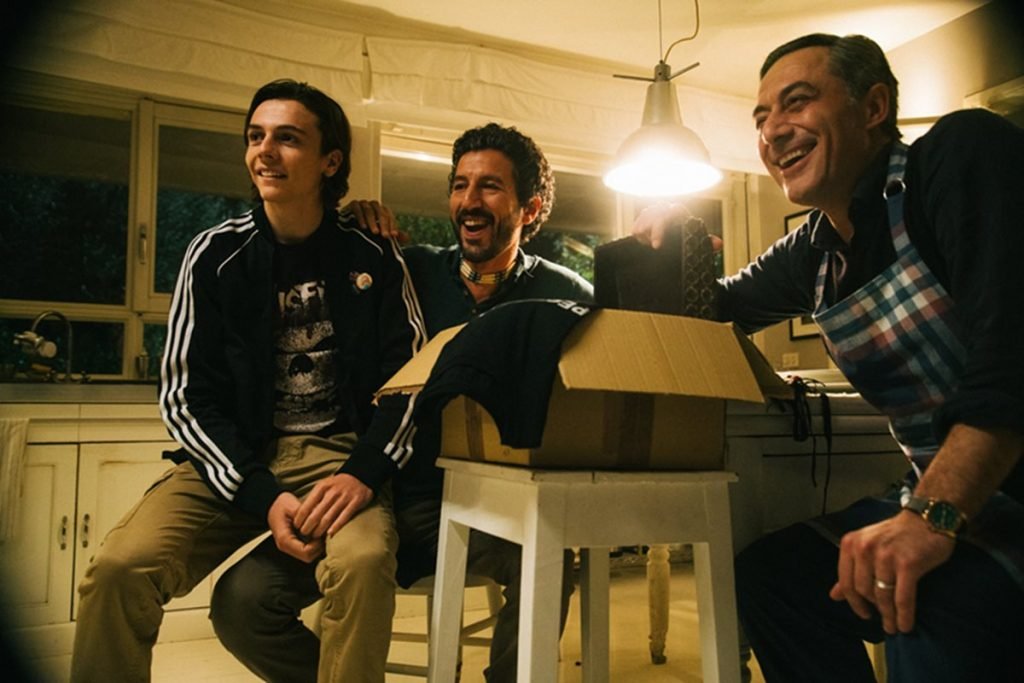 foto de dois homens sentados e um deles com um adolescente no colo