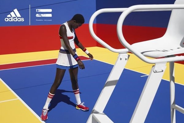 Campanha de divulgação de uma coleção do cantor Pharrell Williams com a marca Adidas. Na foto, uma modelo negra, magra e jovem veste roupas tradicionais de quem joga Tênis. Ela usa uma blusa branca, uma saia plissada branca, meia branca alta e um tênis vermelho.