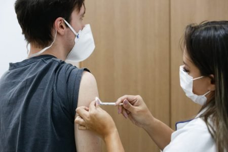 Foto colorida: homem de costas durante aplicação de vacinas - Metrópoles
