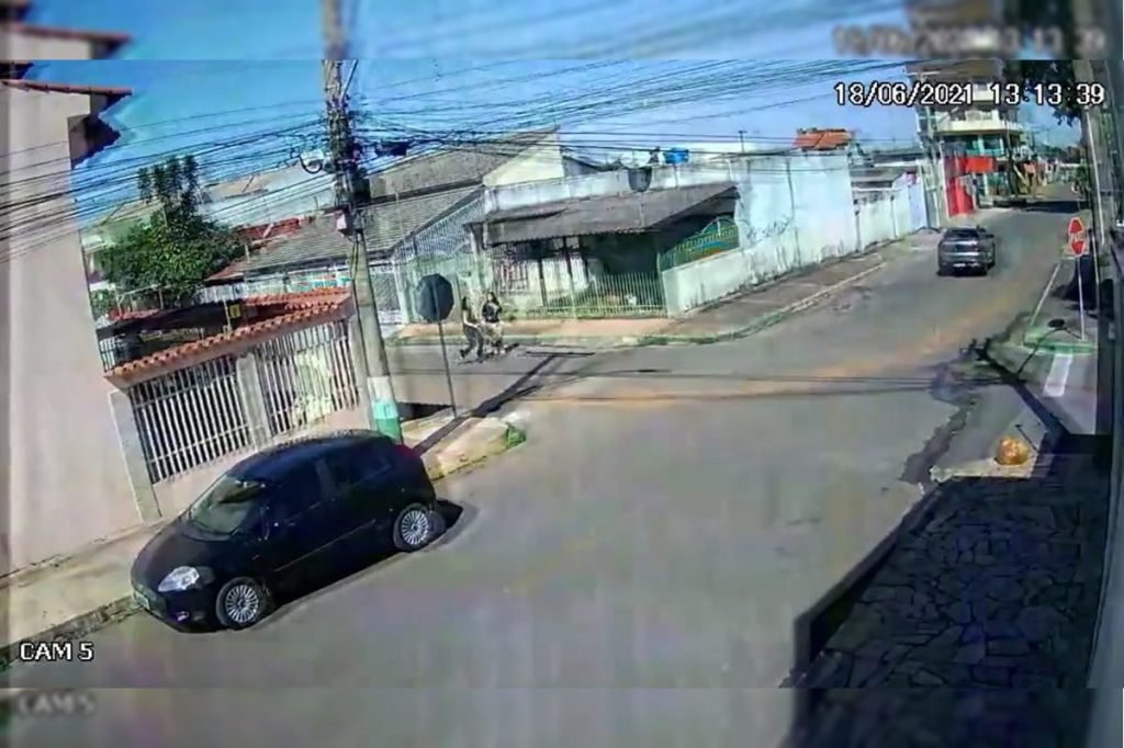 Carro estacionado na rua mulheres correndo atrás de outro carro que está sendo roubado