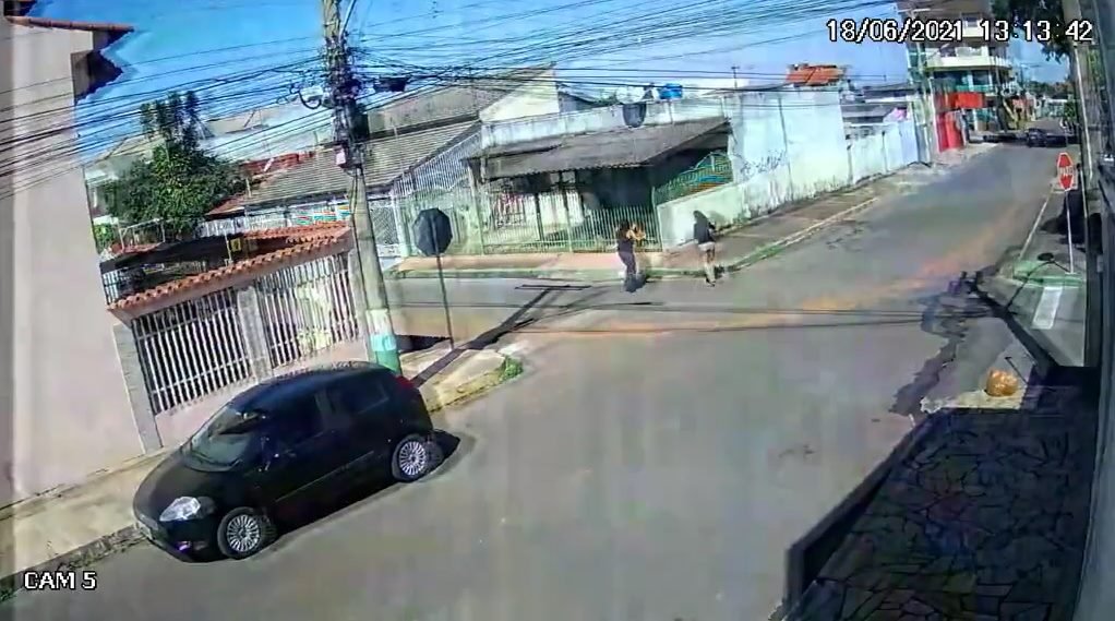 Carro estacionado na rua mulheres correndo atrás de outro carro que está sendo roubado