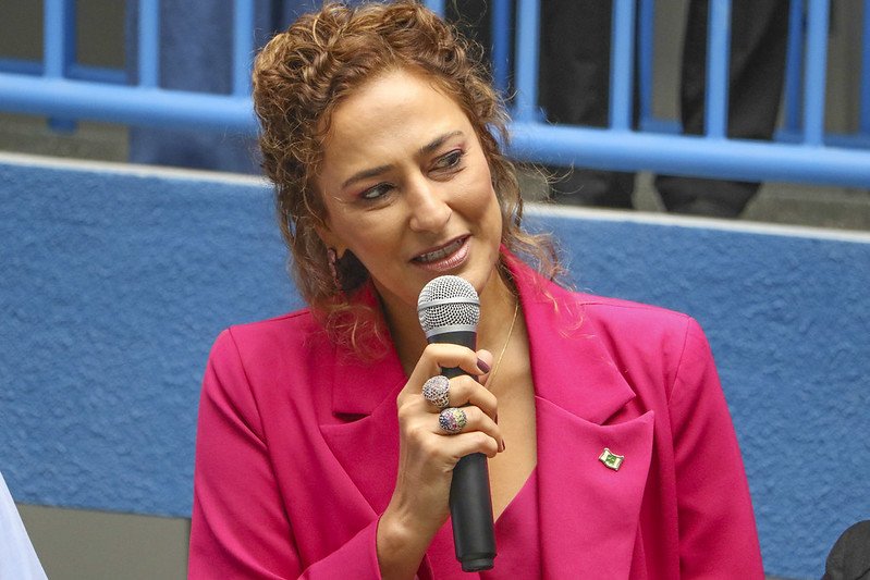 Foto de uma mulher com casaco rosa e microfone na mão