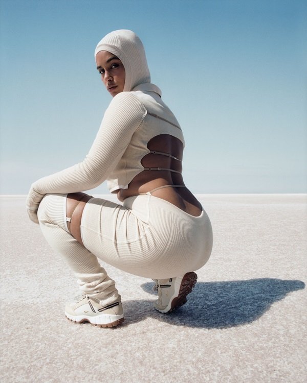 Campanha de divulgação da coleção da Nike em parceria com o estilista francês Simon Jacquemus. Na foto, a cantora Jorja Smith, uma mulher jovem e negra com os cabelos trançados, em dunas de areia branca vestindo roupas também brancas do lançamento.