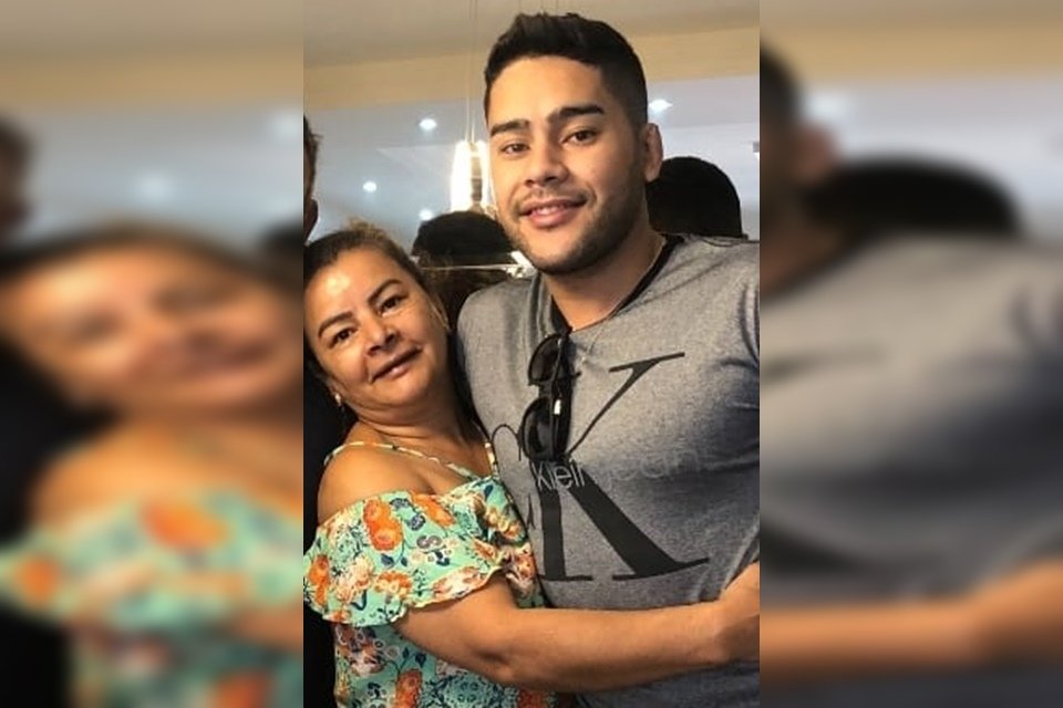 Mulher com vestido florido abraçada com homem com camisa cinza e óculos pendurado na camisa