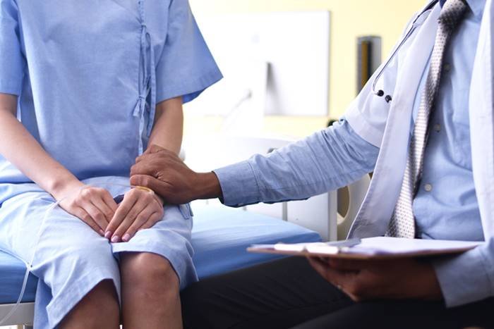 Doctor sitting in front of a woman and with his hand on her arm- Metropolises