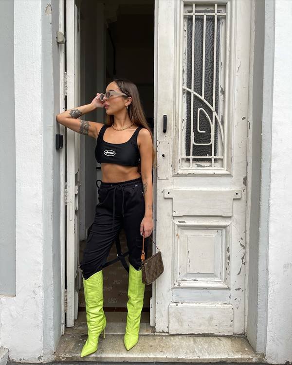 Giovanna Ferrarezi usa top preto, calça preta e bota verde de cano alto 