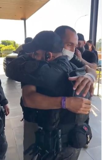 Fotografia colorida de policiais fardados se abraçando