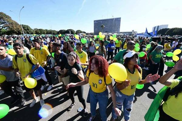 Fotografia colorida de pessoas vestidas de verde e amarelo com balões nas mãos