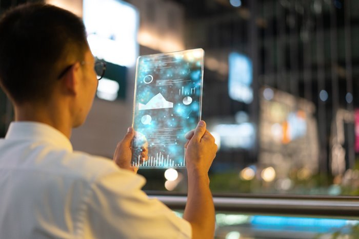 Homem em pé segurando tablet com imagens transparentes - Metrópoles