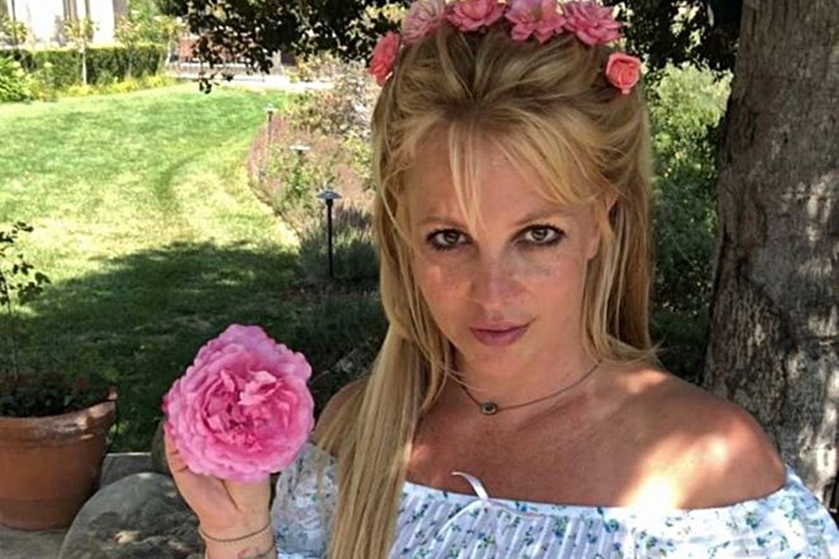 Foto colorida de Britney Spears segurando flor rosa e usando coroa de flores - Metrópoles
