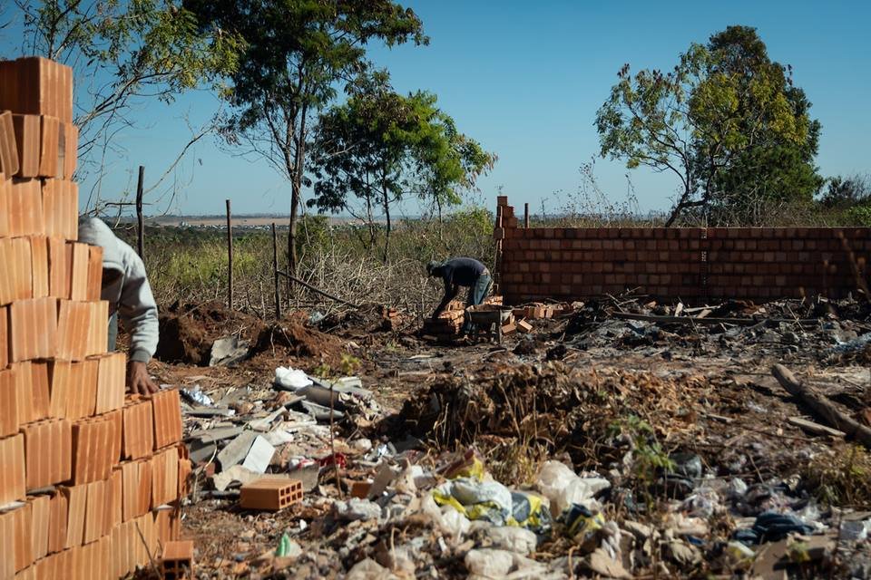 Operários trabalham construindo casas de alvenaria pequenas construídas em descampado numa invasão do Sol Nascente próxima à parque. É possível ver muito lixo na construção - Metrópoles