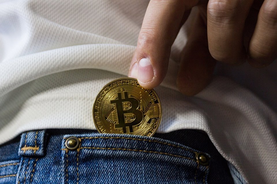 Pessoa colocando moeda Bitcoin no bolso