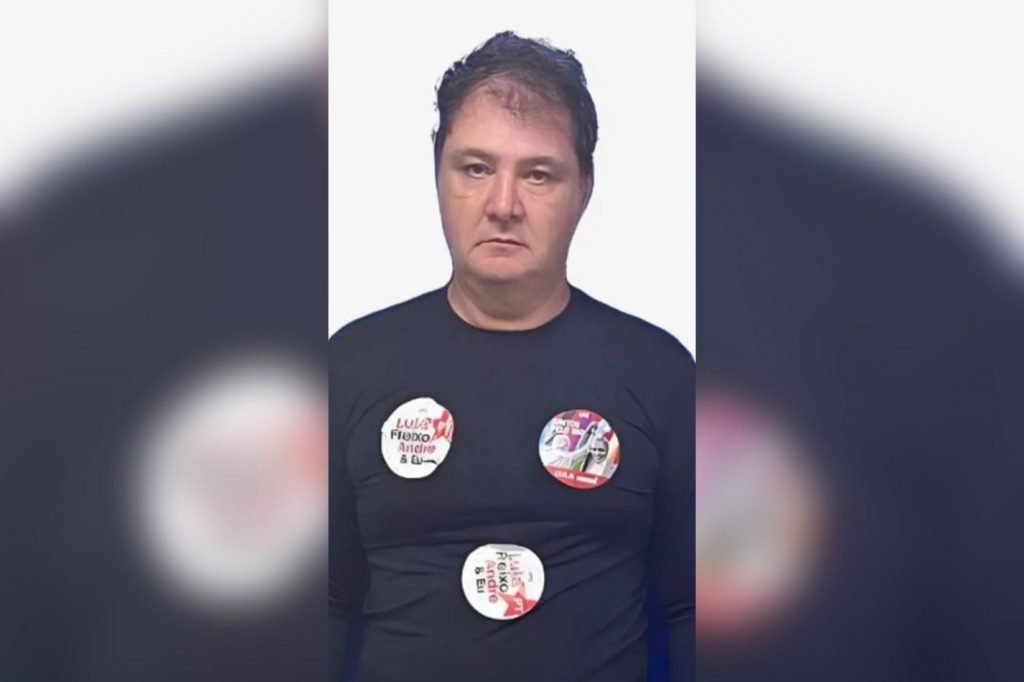 Andre Luiz Stefano Dimitriu Alves, preso em ato pró-Lula na Cinelândia (RJ) por jogar bomba caseira. Na foto ele está preso, diante de fundo branco, e usa camisa preta com adesivos de Lula - Metrópoles