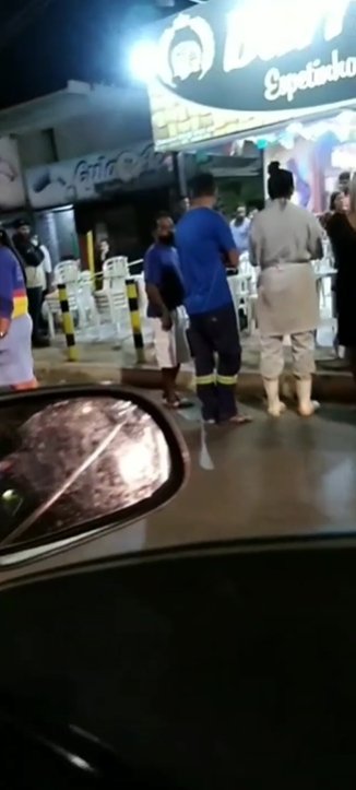 Foto colorida. Multidão observa corpo de homem morto a tiros