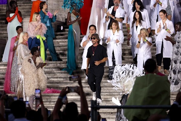 Desfile da Alta-Costura 2022 da Valentino. Na foto, é possível ver as modelos vestindo as roupas da marca e posicionadas nas escadas da praça onde ocorreu a apresentação. No centro, está o estilista Pierpaolo Piccioli, que comanda a etiqueta, um homem branco, de meia idade, e cabelos médios lisos - Metrópoles