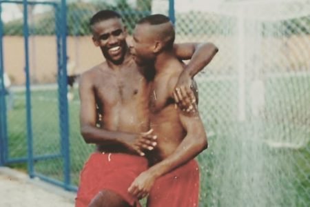 A dupla de funk Claudinho e Buchecha em foto antiga, onde os amigos se abraçam, usando calções vermelhos, em quadra de futebol. A foto foi postada por Buchecha em homenagem aos 20 anos da morte de Claudinho - Metrópoles