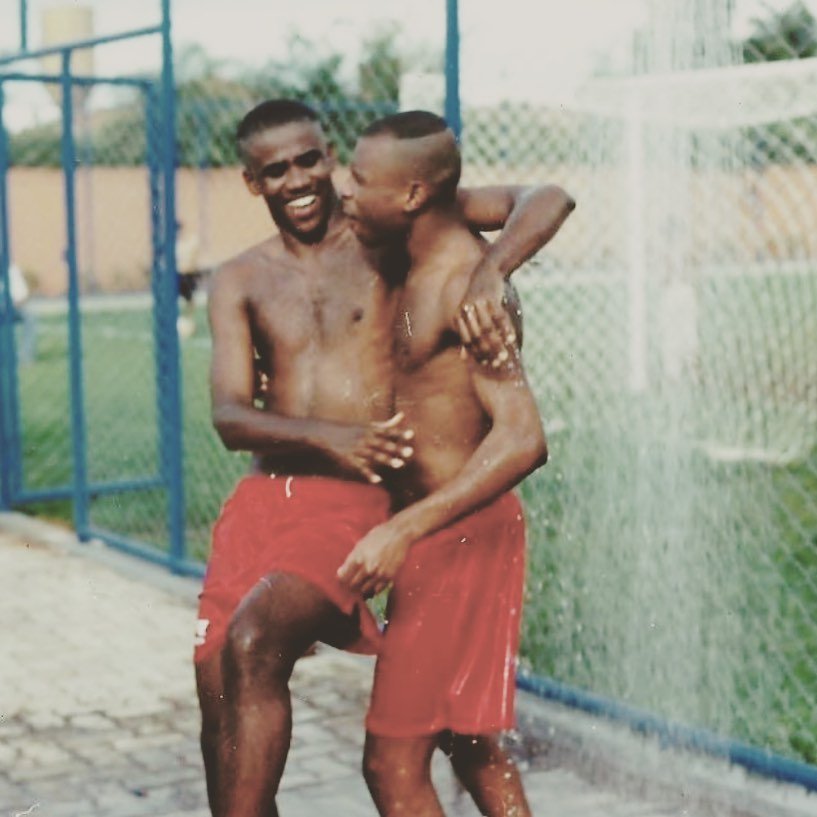 A dupla de funk Claudinho e Buchecha em foto antiga, onde os amigos se abraçam, usando calções vermelhos, em quadra de futebol. A foto foi postada por Buchecha em homenagem aos 20 anos da morte de Claudinho - Metrópoles