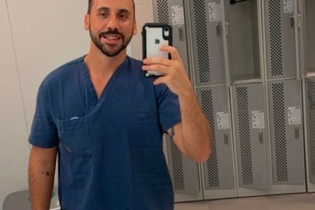 Anestesista Giovanni Quintella Bezerra, flagrado estuprando mulher grávida durante parto, tira foto com seu celular em espelho de vestiário em hospital. Ele usa uniforme médico azul marinho - Metrópoles