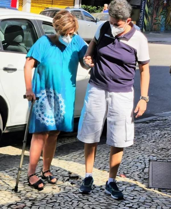Foto colorida de uma mulher ajudando uma senhora a caminhar-Metrópoles