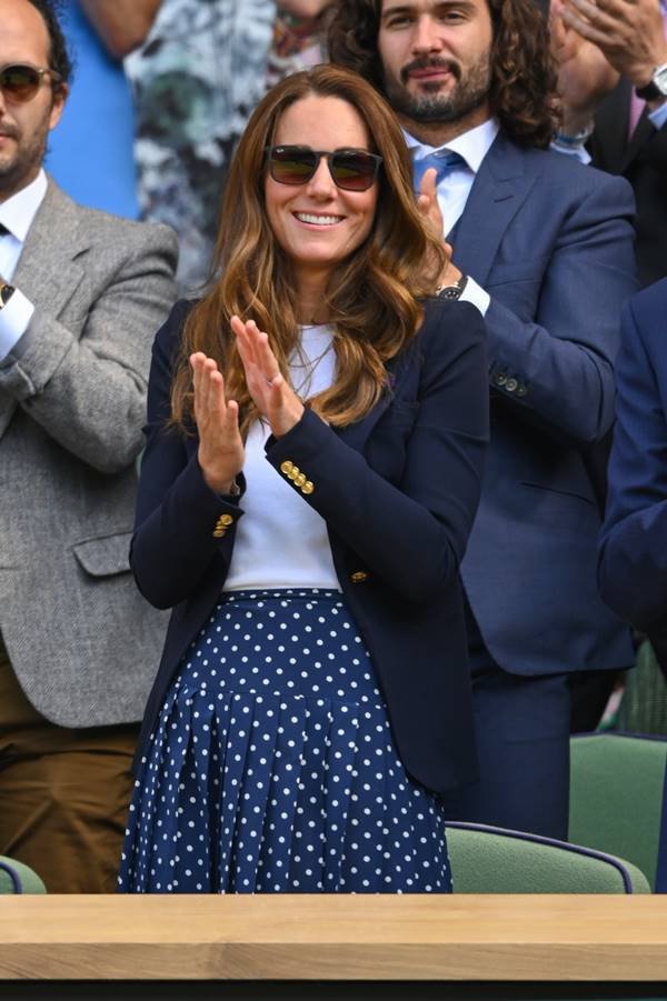 Kate Middleton usando camiseta branca, saia de poá e blazer azul escuro