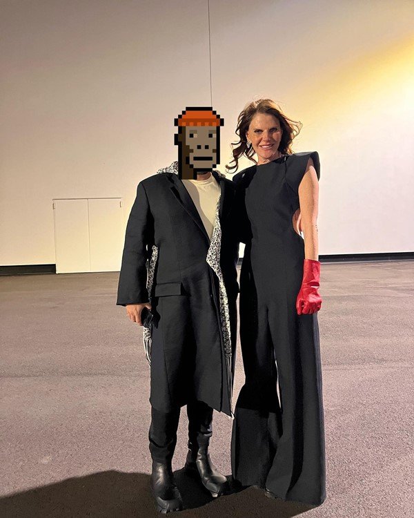 O investidor de NFT GMoney, um homem branco e jovem que esconde sua identidade com o desenho de um emoji pixelado de macaco. Na foto, ele está com uma roupa toda preta e posa ao lado da editora de moda Anna Dello Russo, uma mulher branca e loura de meia idade