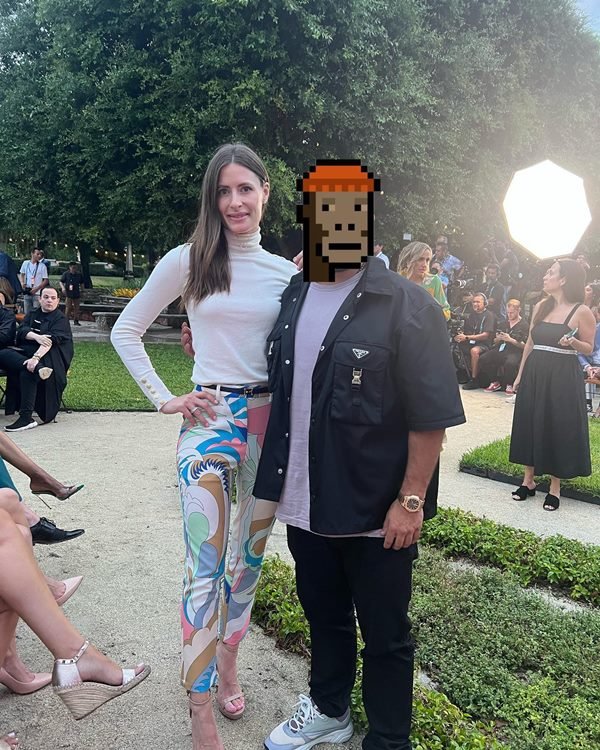 O investidor de NFT GMoney, um homem branco e jovem que esconde sua identidade com o desenho de um emoji pixelado de macaco. Na foto, ele está com uma camiseta cinza, uma camisa e calpa preta, e posa ao lado de uma mulher branca e jovem com cabelo preto