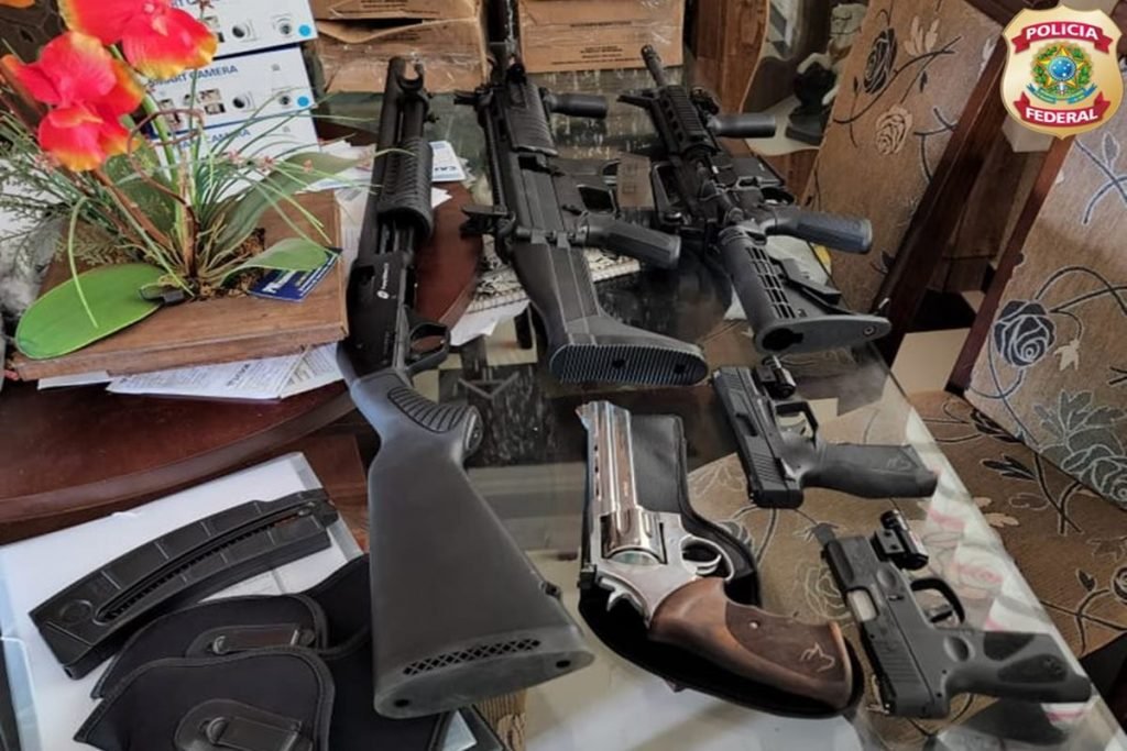 Carabina, pistola, espingarda e outras armas dispostas numa mesa