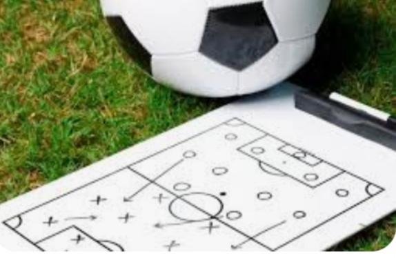 Prancheta com desenho de táticas de futebol ao lado de bola, ambos sob gramado verde - Metrópoles