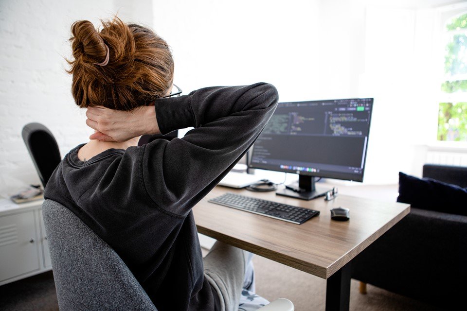 Mulher sentada em frente ao computador com mão no pescoço