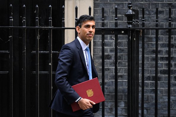 Rishi Sunak, ex-chefe da pasta de Finanças e recém eleito premiê inglês caminha em frente à casa oficial do primeiro-ministro na Downing Street segurando pasta vermelha - Metrópoles