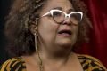 Foto de Babi Cruz. Ela tem pele negra, usa óculos de grau, uma blusa de oncinha, tem cabelos longos e cacheados e parece emocionada - Metrópoles